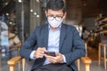 Young Businessman in suit wearing surgical face mask and using smartphone, man typing touchscreen mobile phone in office or cafe. Royalty Free Stock Photo