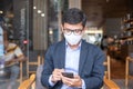 Young Businessman in suit wearing surgical face mask and using smartphone, man typing touchscreen mobile phone in office or cafe. Royalty Free Stock Photo