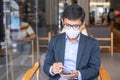 Young Businessman in suit wearing surgical face mask and using smartphone, man typing touchscreen mobile phone in office or cafe. Royalty Free Stock Photo