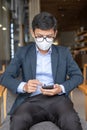 Young Businessman in suit wearing surgical face mask and using smartphone, man typing touchscreen mobile phone in office or cafe. Royalty Free Stock Photo