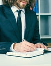 Young businessman in suit working at office, sitting at desk and writing notes for personal organizer. Royalty Free Stock Photo