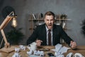 Young businessman in suit yelling while sitting at messy workplace