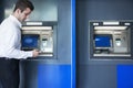 Young businessman taking out money from the ATM and looking down at his phone Royalty Free Stock Photo