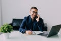 Young businessman talking on cell phone and using laptop in office Royalty Free Stock Photo