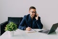 Young businessman talking on cell phone and using laptop in office Royalty Free Stock Photo