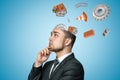 Young businessman thinking with white houses, gear wheels, bricks and traffic cone flying out of his head on blue Royalty Free Stock Photo