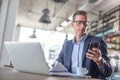 Young businessman types on his mobile phone with a laptop and coffee in front of him in a coffee shop