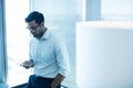 Young businessman using mobile phone while leaning on glass window Royalty Free Stock Photo