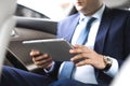 Young businessman using tablet pc while sitting on back seat of a car. Caucasian male business executive by a taxi and looking at Royalty Free Stock Photo