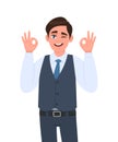 Young businessman in waistcoat showing okay or OK gesture and winking eye. Person making symbol of good or cool sign.