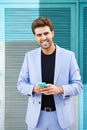 Young businessman wearing blue suit using a smartphone in urban background.