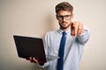 Young businessman wearing glasses working using laptop standing over white background pointing with finger to the camera and to Royalty Free Stock Photo