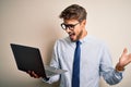 Young businessman wearing glasses working using laptop standing over white background very happy and excited, winner expression Royalty Free Stock Photo