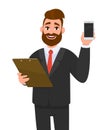 Young businessman wearing a suit holding clipboard and showing new digital mobile, cell or smartphone. Person keeping the file pad Royalty Free Stock Photo