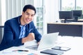 A young businessman wearing a suit and a long sleeve shirt inside and sitting smart poses has a feel happy smile in a modern