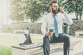 Young businessman in white shirt and tie is sitting outside on bench,drinking coffee and talking on his cell phone. Royalty Free Stock Photo