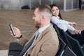 Young businessman and woman waiting at airport lounge. Man looking at phone. Business travelers waiting for their flight Royalty Free Stock Photo