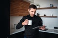 Young businessman work in kitchen. Entrepreneur stand alone, hold tablet and look at it. Businessman has productive day Royalty Free Stock Photo