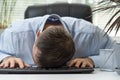Young businessman working at computer, falling asleep in office on keyboard. Tired and fatigued office worker sleeping on desk Royalty Free Stock Photo