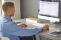 Young businessman working in office, sitting at desk, looking at laptop computer screen, smiling