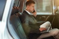 Young businessman works in his laptop having business phone conversation while sitting in his car on his way to office, Royalty Free Stock Photo