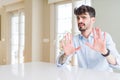 Young businesss man sitting on white table afraid and terrified with fear expression stop gesture with hands, shouting in shock