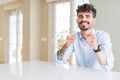 Young businesss man sitting on white table pointing fingers to camera with happy and funny face Royalty Free Stock Photo