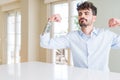 Young businesss man sitting on white table showing arms muscles smiling proud