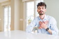 Young businesss man sitting on white table smiling with hands on chest with closed eyes and grateful gesture on face