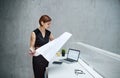 Young businesswoman or architect with blueprints and laptop standing in office. Royalty Free Stock Photo