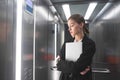 Young businesswoman is concentrated on lookinig at the floor number in the elevator holding her laptop. Female office worker in