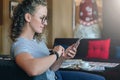 Young businesswoman with curly hair in glasses sits, uses smartphone, working. Hipster girl is blogging, checking email. Royalty Free Stock Photo