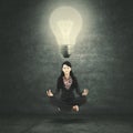 Businesswoman meditating under a bright bulb