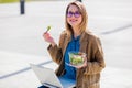 Young businesswoman eating salad and working with computer at urban outdoor