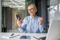Young businesswoman, freelancer sitting in the office at the desk with a laptop, and looking at the mobile phone Royalty Free Stock Photo