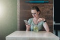 Young businesswoman in glasses sits in a cafe at table, drinks beverage and uses smartphone. Royalty Free Stock Photo