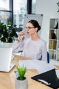 Young businesswoman in glasses, sitting at desk in modern office and drinking glass Royalty Free Stock Photo