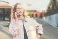 Young businesswoman in glasses is standing on a city street and talking on cell phone. Backlight, sunset.