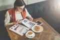 Young businesswoman in glasses and white sweater is sitting in cafe at table, working.Businesswoman is looking at charts Royalty Free Stock Photo