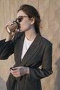 Young businesswoman is having breakfast in the park. Girl in sunglasses drinks soy coffee from recycled paper cups Royalty Free Stock Photo