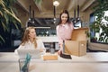 Young businesswoman holding box of personal belongings about to leave office after quitting job