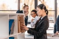 Young businesswoman holding folder while colleagues standing and looking behind Royalty Free Stock Photo