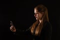Young businesswoman holding a mobile phone in darkness illuminated from behind. Royalty Free Stock Photo