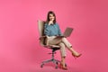 Young businesswoman with laptop sitting in comfortable office chair on pink background Royalty Free Stock Photo