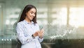 Young businesswoman in a light blue shirt uses her smartphone, with digital financial graphics Royalty Free Stock Photo