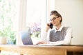 Young businesswoman making a phone call and using laptop while working from home Royalty Free Stock Photo