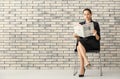 Young businesswoman reading newspaper against brick wall Royalty Free Stock Photo