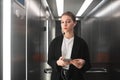 Young businesswoman is seriously looking at the camera in elevator using her smartphone and headphones. Portrait of female Royalty Free Stock Photo