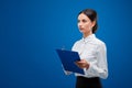 Young businesswoman seriously thinking about an idea while holding a blue clipboard, on blue background