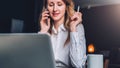 Young businesswoman in shirt is sitting in office at table in front of computer, talking on cell phone Royalty Free Stock Photo